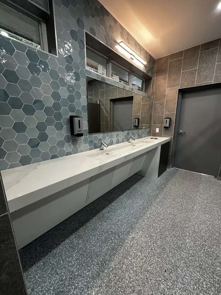 Detailed view of the sink area featuring large frameless mirrors and warm integrated lighting that highlights the textured wall tiles.