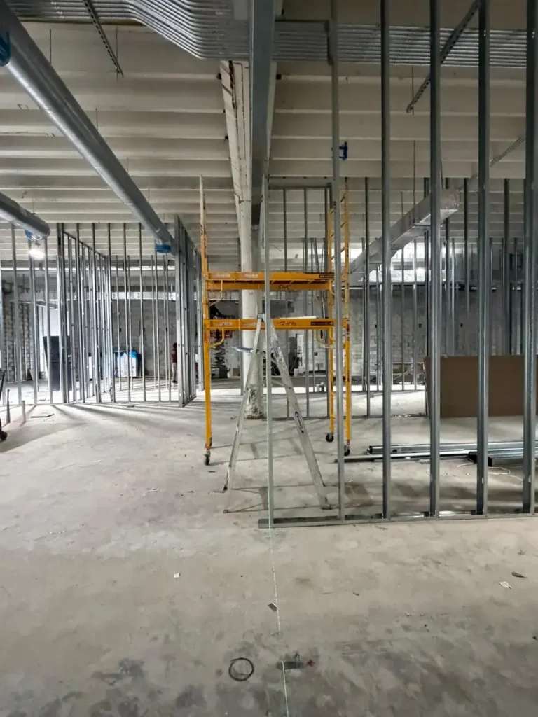 Metal stud wall partitions under construction in a commercial building with HVAC and electrical systems installed above.